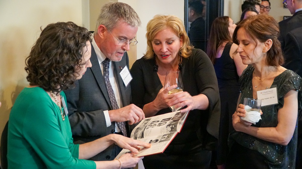 Four McGovern Medical School alumni looking at a photo album at Alumni Weekend event