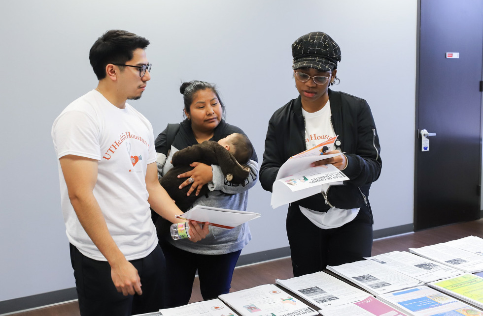 Community members reviewing health education materials at an outreach event, one person holding a baby.